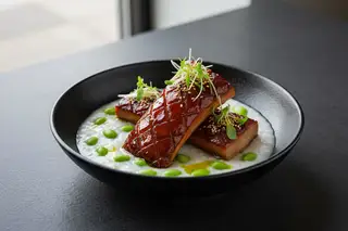 Char Siu King Oyster 'Bone Marrow' with Truffle Edamame Congee Glazed Char Siu King Oyster 'bone marrow' over creamy truffle edamame congee in a matte black bowl, garnished with micro-shiso.