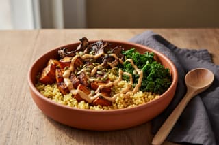 Scorched harissa sweet potato and millet brunch bowl in a terracotta dish with peanut sauce on a rustic wooden table in soft morning light.