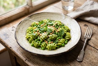 Spring Pea and Preserved Lemon Tonnarelli A minimalist plate of bright green spring pea pasta with pine nuts and mint on a rustic wooden table.