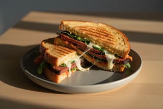 Toasted sourdough miso-melt with smoky tempeh brisket, melted vegan cheese, and red kimchi on a grey plate under warm golden-hour light.