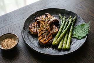 Grilled glazed king oyster mushrooms and asparagus on a dark ceramic plate, minimalist Japanese setting.