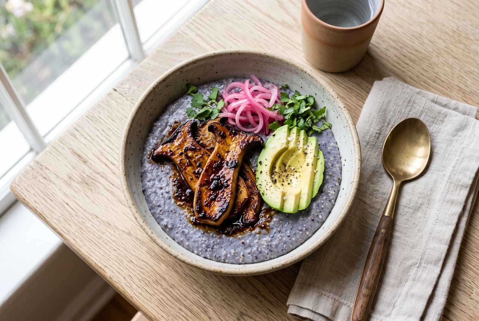 Smoked King Trumpet and Heirloom Masa Umami Bowl Savory vegan breakfast bowl with glazed mushrooms, avocado, and pickled onions on a base of heirloom masa, served on a sunlit wooden table.