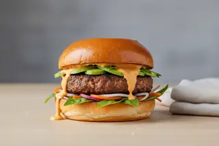 Gourmet vegan burger: mushroom-walnut patty, gochujang cream, pickled daikon and Thai basil on a golden brioche bun. Minimalist food photography.