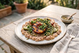 Charred Peach and Nopal Asado with Smoky Pinto Mash and Preserved Lemon Gremolata Grilled peaches and nopales on smoky pinto beans with herb gremolata on a white plate in soft sunlight.