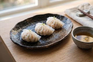 Three translucent vegan dumplings with green citrus zest on a grey handmade ceramic plate, arranged in a minimalist Japanese style.