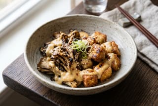 A minimalist presentation of grilled maitake and tofu in a creamy miso sauce on a textured grey ceramic plate.