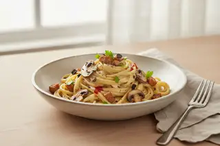 Gourmet vegan miso carbonara with linguine, shiitake, tempeh bacon, and black garlic, drizzled with chili oil in a minimalist ceramic bowl.