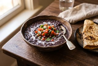 Swahili Coast Njahi and Coconut Velvet Stew A bowl of velvety njahi bean stew with coconut milk and fresh kachumbari garnish on a wooden table.