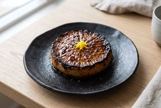 Charred daikon roast with dark miso glaze on a handmade ceramic plate, garnished with yuzu zest in a minimalist Japanese setting.