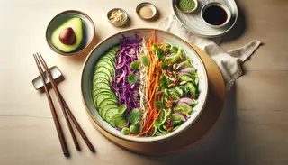 Vegan Asian fusion salad in a white bowl on a light wood table, with avocado slices, cilantro, and chopsticks.