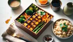 Image shows a caramelized bento box with brown rice, tofu, sweet potato, and broccoli on a minimalist table. No people or text visible.