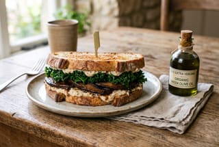 Braised Portobello and Cavolo Nero Panino with Cannellini Crema A rustic gourmet vegan sandwich with braised mushrooms and kale on sourdough bread, served on a wooden table.