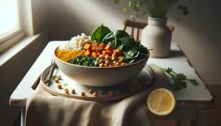 African Vegan Brunch Bowl with millet, sautéed sweet potatoes, chickpeas, spinach, peanuts, and coriander on a minimalist table, with a lemon wedge.