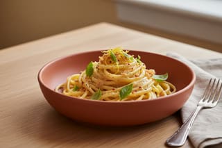 Zesty vegan lemon-miso linguine in a terracotta bowl, topped with Thai basil and gochugaru on an oak table in soft natural light.