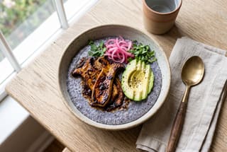Smoked King Trumpet and Heirloom Masa Umami Bowl Savory vegan breakfast bowl with glazed mushrooms, avocado, and pickled onions on a base of heirloom masa, served on a sunlit wooden table.