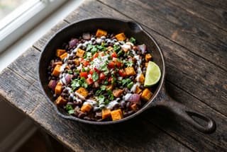 A rustic skillet filled with spiced black beans, sweet potatoes, and fresh kachumbari garnish on a simple wooden table in soft morning light.