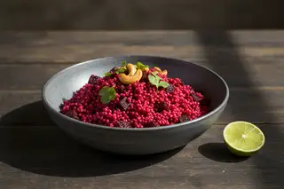 Smoked Beetroot and Fonio Pilau Vibrant magenta smoked beetroot and fonio pilau with toasted cashews in a rustic bowl. Minimalist African-inspired vegan gourmet culinary photography.