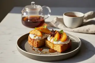 Vegan panettone with miso-tofu cream and Earl Grey peaches, garnished with star anise and sesame on a sunlit minimalist marble table.