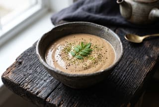 Sansho-Scented Coffee and Silken Tofu Cream A mocha-toned tofu cream in an earthy ceramic bowl, dusted with pepper and garnished with a green leaf on a dark wooden table.