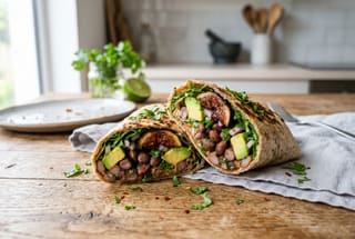 Smoky Late-Summer Harvest Wrap A sliced vegan wrap filled with smoky beans, grilled figs, and avocado on a wooden table in soft natural light.