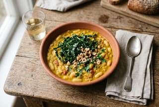 A vibrant golden bean and kale curry served in a rustic bowl on a wooden table.