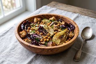 A warm roasted salad with charred radicchio, fennel, and sourdough croutons in a wooden bowl on a linen cloth.