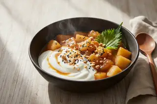 Miso-ginger glazed orchard fruit stew with coconut yogurt, hazelnuts, and shiso in a dark ceramic bowl. Minimalist Italian-Japanese fusion.