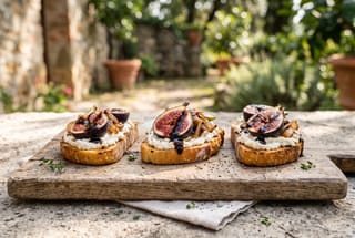 Syrupy Balsamic Fig and Caramelized Shallot Crostini Three vegan fig and shallot crostini with balsamic glaze on a rustic wooden board under natural sunlight.