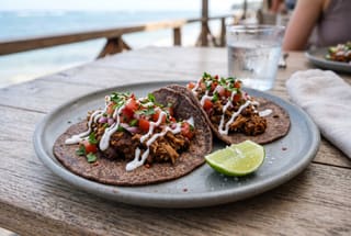Three vegan Swahili-style tacos on a ceramic plate, featuring dark spiced beans, jackfruit, and fresh tomato salsa.