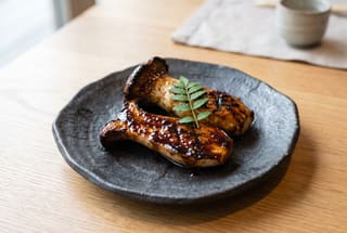 Binchotan Grilled Eringi with Sticky Miso-Tamari Reduction Grilled king oyster mushrooms with a glossy dark glaze on a textured grey ceramic plate, minimalist and clean aesthetic.