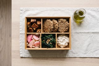 Tuscan Fermented Farro Bento Box A wooden bento box filled with balsamic glazed tempeh, fermented farro cakes, colorful pickled vegetables, wilted kale, and cultured ricotta.