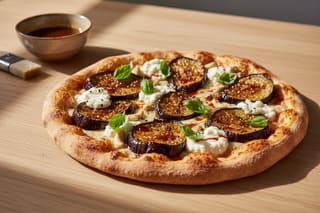 Miso-maple eggplant pizza with almond ricotta, Thai basil, and chili oil on a charred crust, set on a light wood table in soft sunlight.