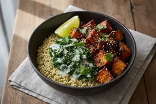 Miso-glazed sweet potato bowl with coconut Sukuma Wiki and teff grains in a dark clay bowl, garnished with sesame and lime.