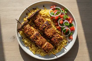 Suya-Spiced King Oyster Mushrooms with Millet and Kachumbari Vegan Suya King Oyster skewers on golden millet with fresh Kachumbari salad. Top-down view of African plant-based fusion on a minimalist plate.