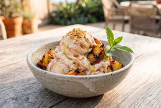 Vegan peach ice cream with grilled fruit and toasted masa in a matte bowl on oak, bathed in warm coastal California golden hour sunlight.