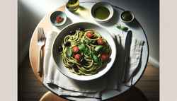 Image of vegan Thai basil pesto pasta with cherry tomatoes, black olives, and red pepper flakes on a white plate, set on a wooden table with a fork and napkin.