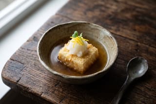 Binchotan-Seared Agedashi Tofu in Yuzu-Kombu Shizuku Crispy agedashi tofu in clear golden dashi, topped with grated daikon and yuzu zest in a rustic ceramic bowl.