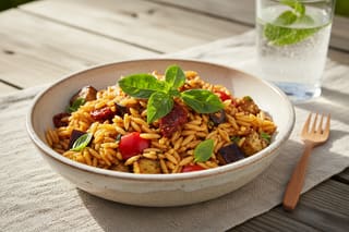 Miso-glazed Sicilian orzo salad with eggplant and Thai basil in a cream bowl on a sunlit rustic table. Elegant vegan European-Asian picnic.