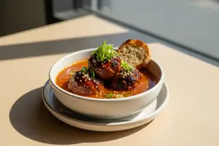Charred vegan BBQ albondigas in a red gochujang-miso broth with scallions and sesame seeds, reflecting warm California sunlight.