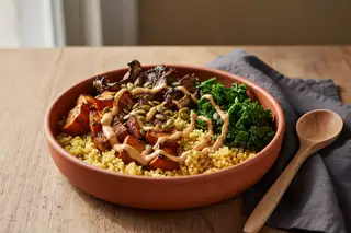 Scorched harissa sweet potato and millet brunch bowl in a terracotta dish with peanut sauce on a rustic wooden table in soft morning light.