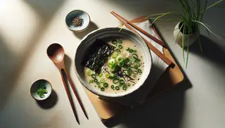Asian-inspired vegan miso soup in a light bowl on a wooden table, with chopsticks and a spoon, garnished with green onions and nori.
