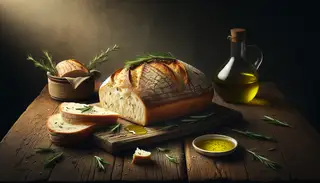 Image of rosemary olive oil bread on a wooden table, with rosemary on the crust, next to an olive oil dish, in soft, inviting light.