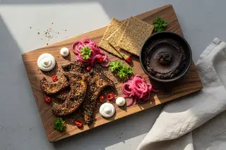 Plant-based African platter: Suya mushrooms, heritage grain crackers, and hibiscus pickles on a dark wood board in soft natural light.