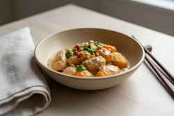 Vegan Ginger-Miso Pumpkin Gnocchi topped with Thai basil pesto and chili oil, served in a ceramic bowl with chopsticks on a wood table.