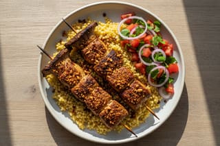 Vegan Suya King Oyster skewers on golden millet with fresh Kachumbari salad. Top-down view of African plant-based fusion on a minimalist plate.