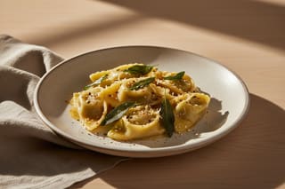 Miso-roasted fennel agnolotti with ginger-sage glaze and shichimi togarashi on a minimalist plate in soft, natural Mediterranean light.