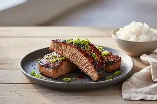 Vegan Gochujang Lion's Mane BBQ steaks with a crimson glaze, scallions, and sesame seeds on a charcoal plate in golden sunlight.