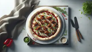 Artisan vegan pizza with hoisin sauce, jackfruit, and vegan mozzarella, garnished with green onions, sesame, chili flakes, and cilantro on a clean table.