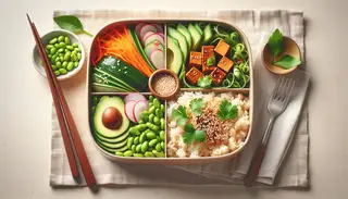 Image of a minimalist table setting with a 'Grassy Bento Box' containing brown rice, colorful vegetables, tofu, edamame, sesame seeds, cilantro, and pickled ginger.