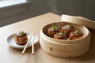 Smoky Seitan Siu Mai with Gochujang BBQ Glaze Vegan Seitan Siu Mai with glossy Gochujang BBQ glaze in a bamboo steamer, topped with cilantro and sesame in bright, sunny California light.